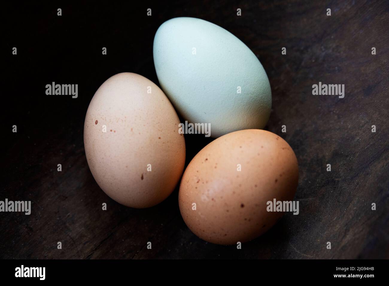 Tres huevos de pollo frescos y coloridos en un tazón rústico de madera. Foto de stock