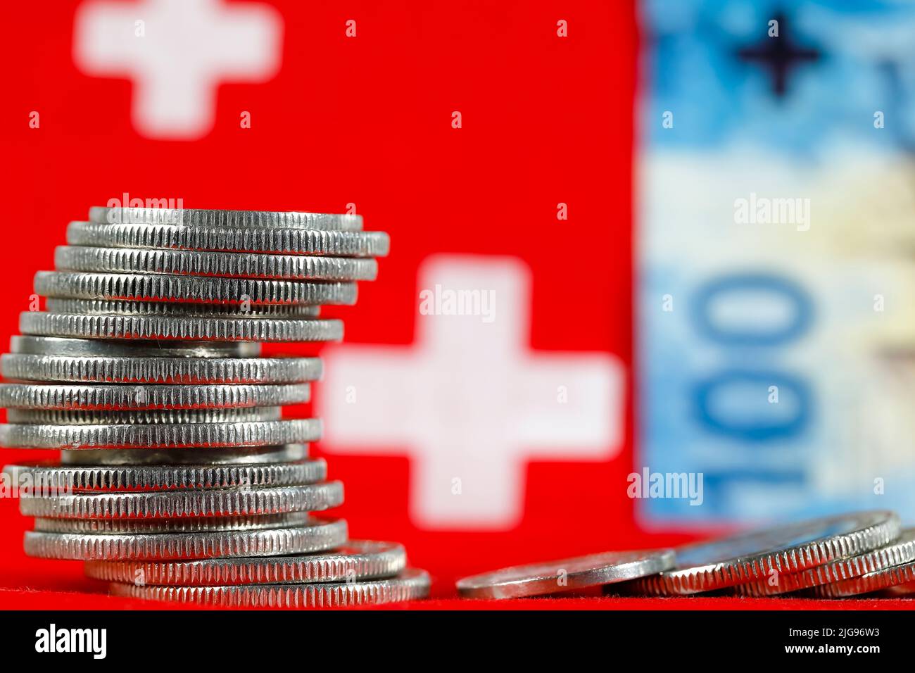 Aquí hay un grupo de monedas suizas y en el fondo hay un billete y hay símbolos de la bandera suiza. Foto de stock