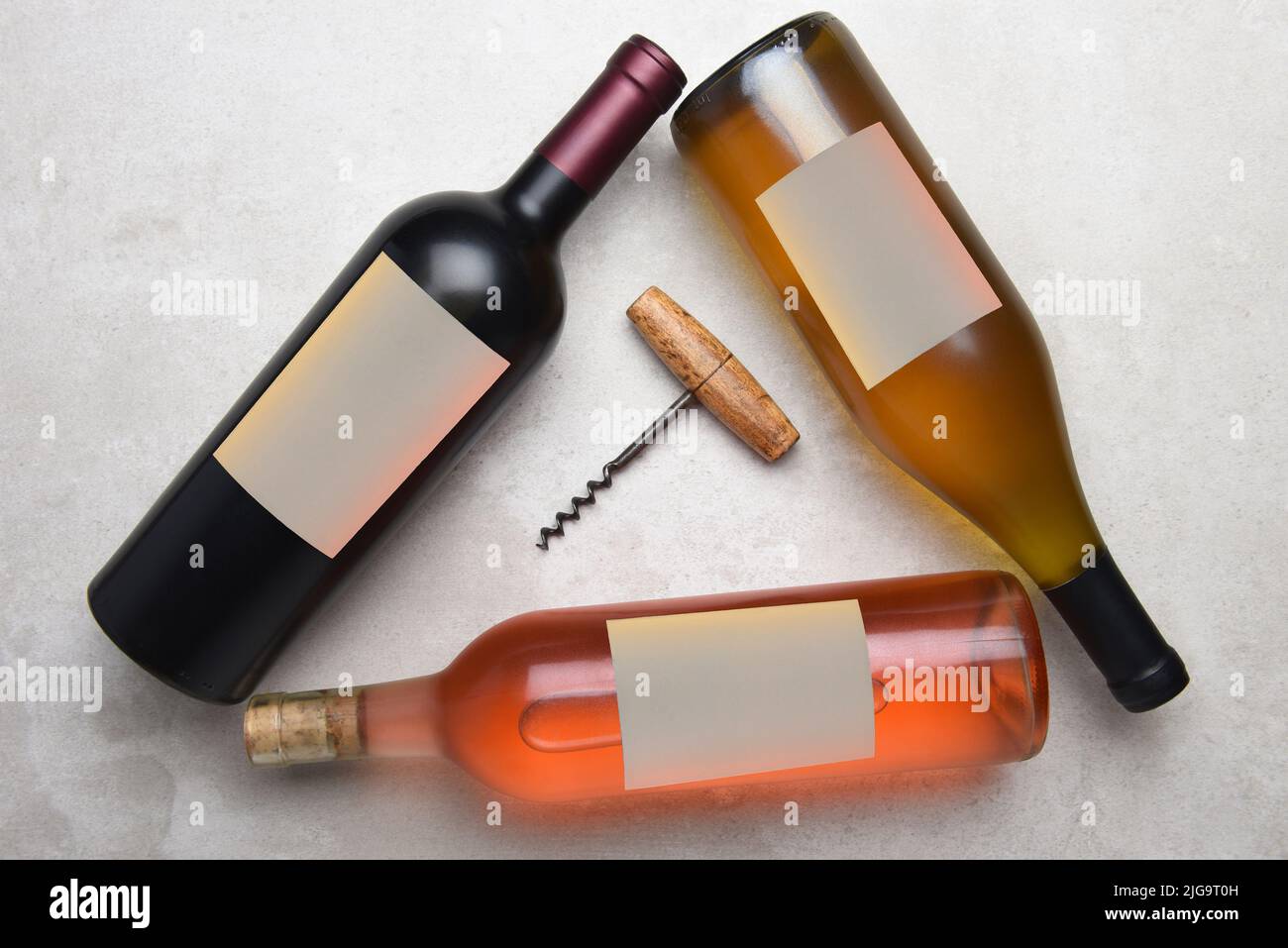Cabernet, Rose, Chardonnay: Vista aérea de un grupo de tres botellas diferentes con etiquetas en blanco dispuestas en un triángulo con un sacacorchos en el midd Foto de stock