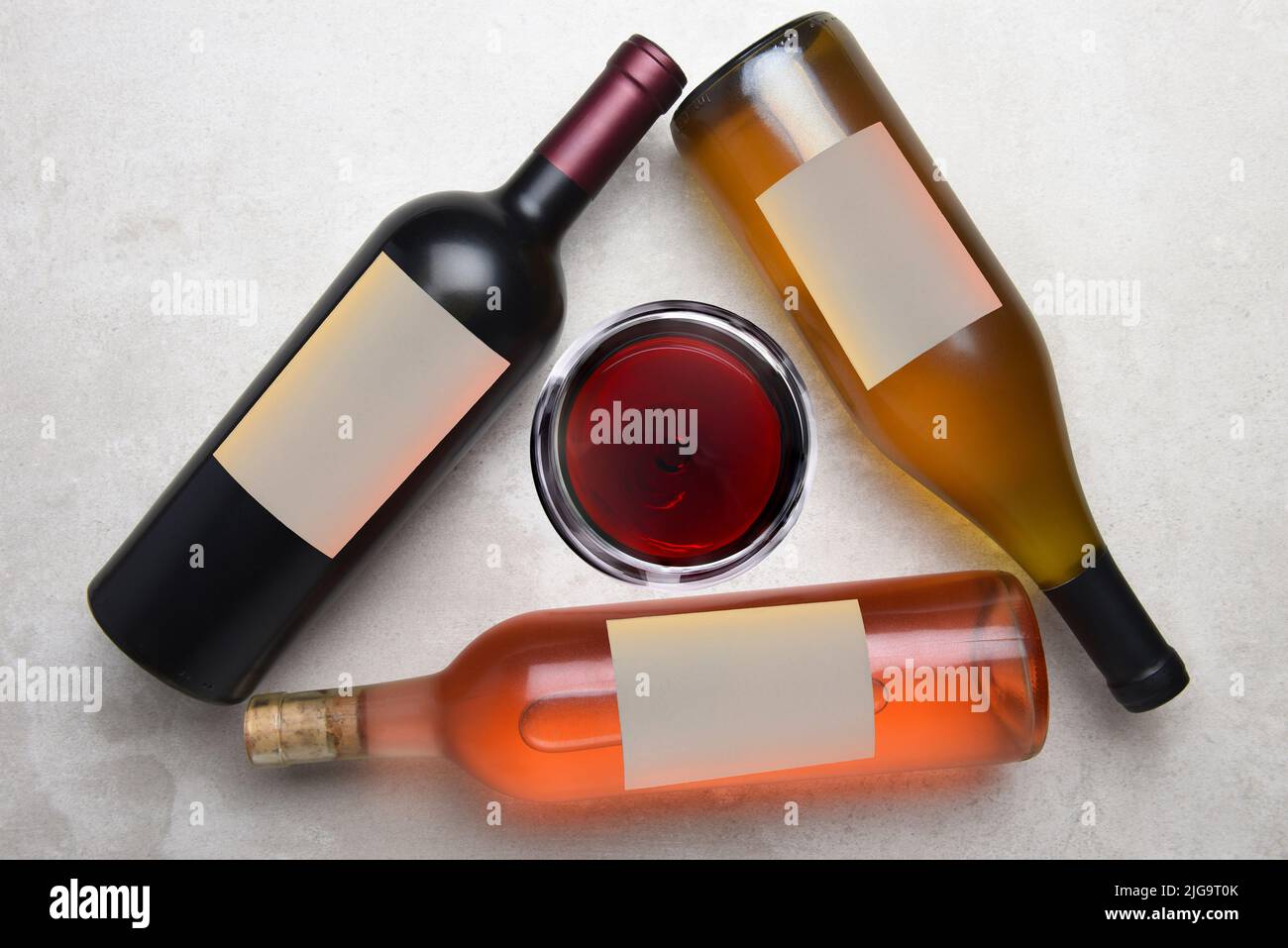 Cabernet, Rose, Chardonnay: Vista aérea de un grupo de tres botellas diferentes con etiquetas en blanco dispuestas en un triángulo con una copa de vino en el m. Foto de stock