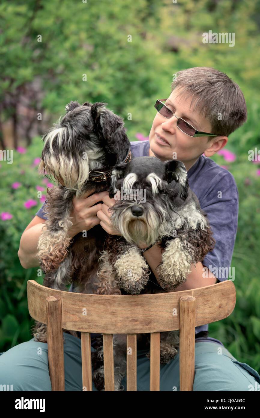 Mujer sentada al aire libre con dos perros en miniatura schnauzer Foto de stock