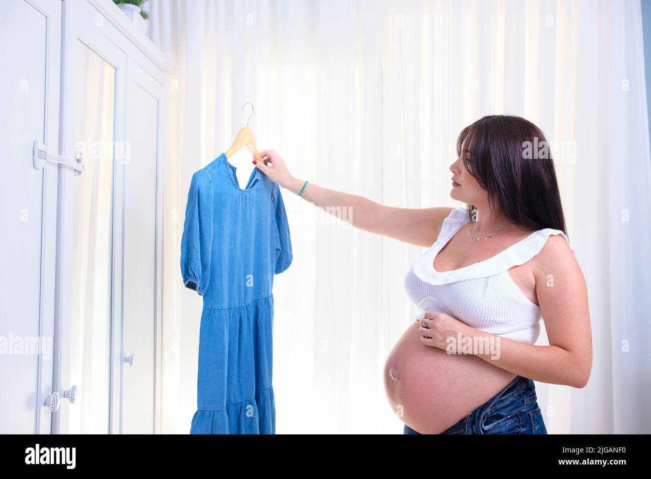 Mujer joven embarazada que elige qué ropa usar. Foto de stock