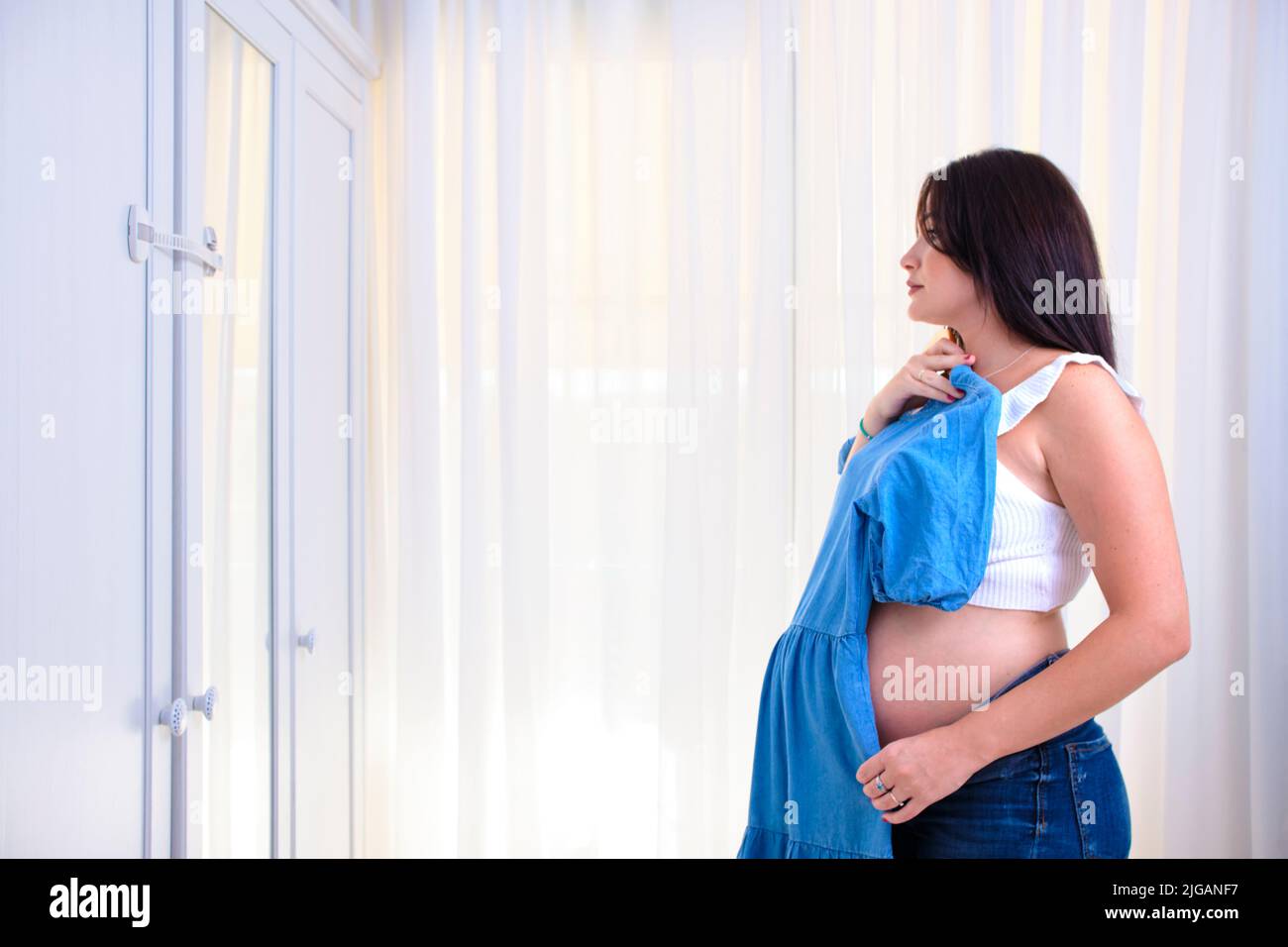 Mujer joven embarazada que elige qué ropa usar. Foto de stock