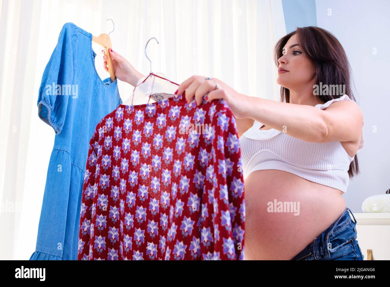 Mujer joven embarazada que elige qué ropa usar. Foto de stock