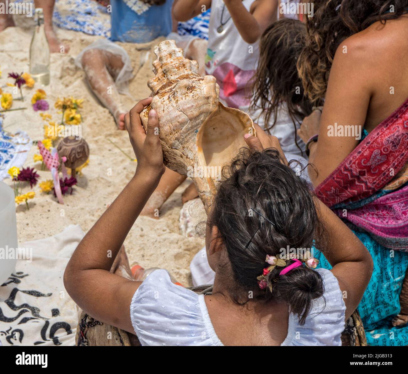 Una joven mujer espiritual en la playa sopla en una concha de mar durante una ceremonia de grupo Foto de stock
