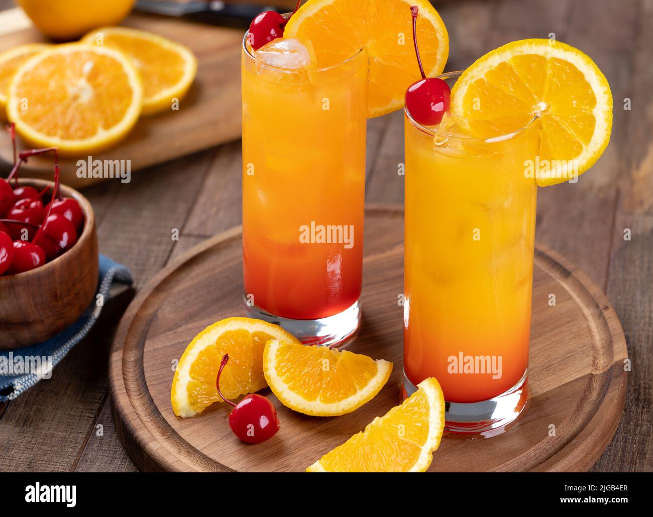 Cóctel Tequila Sunrise con rodaja de naranja y cereza sobre una mesa rústica de madera Foto de stock