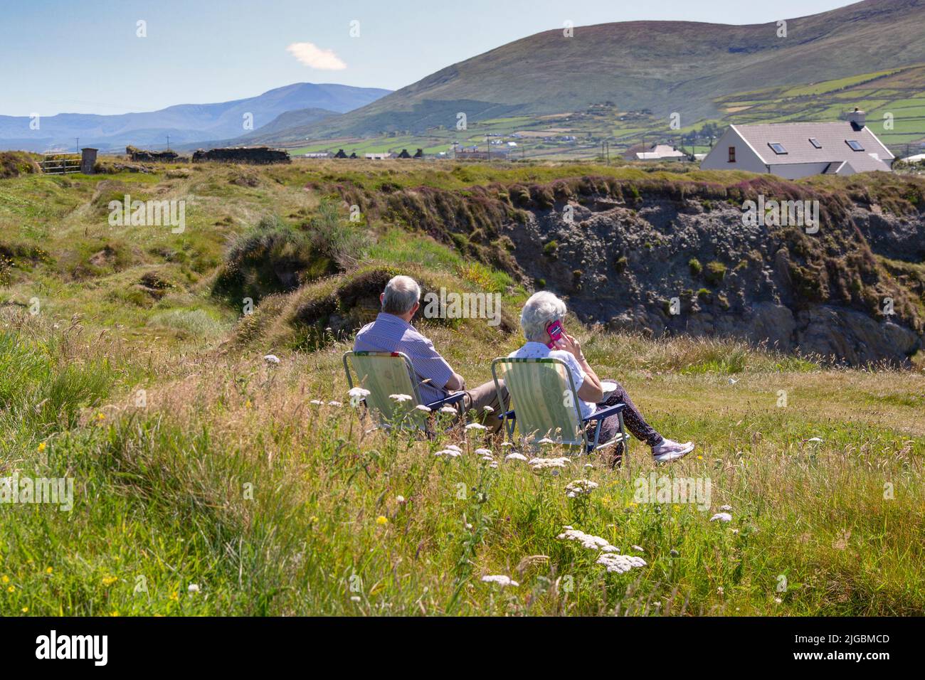 Pareja mayor sentada en sillas de jardín en hierba larga, Isla Valentia, Kerry, Irlanda Foto de stock