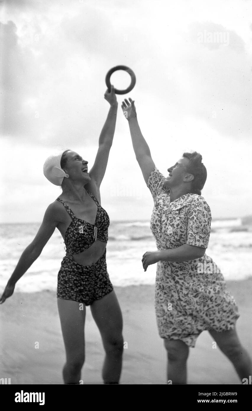 1950s, histórico, dos mujeres divirtiéndose en una playa, una mujer en un traje de baño de 2 piezas de la época, sosteniendo un anillo de goma, con la otra dama llegando a tratar de agarrarlo, Inglaterra, Reino Unido. Foto de stock