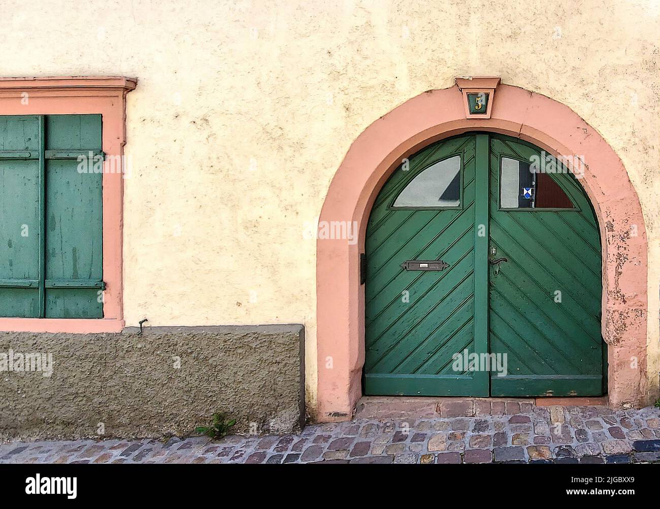 Antigua puerta europea en arco verde con ventanas en una calle de ladrillo Foto de stock