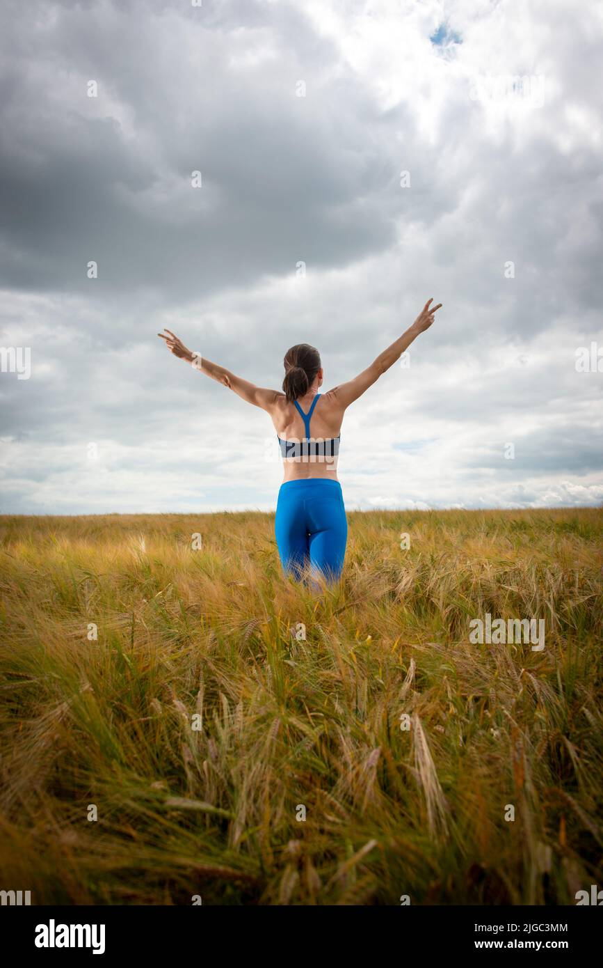 Mujer con los brazos levantados en medio de un campo disfrutando del verano y la naturaleza Foto de stock