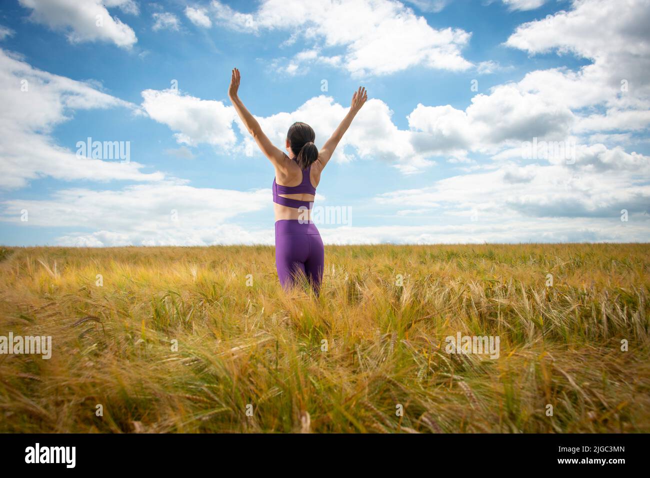 Mujer con los brazos levantados en medio de un campo disfrutando del verano y la naturaleza Foto de stock