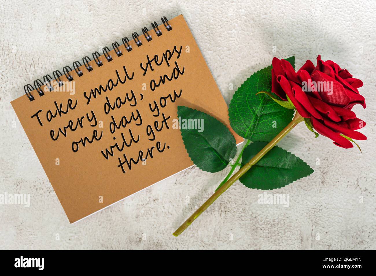 Cita de motivación en un libro de notas marrón con rosas rojas en un escritorio de mármol - da pequeños pasos cada día, y un día llegarás allí. Foto de stock