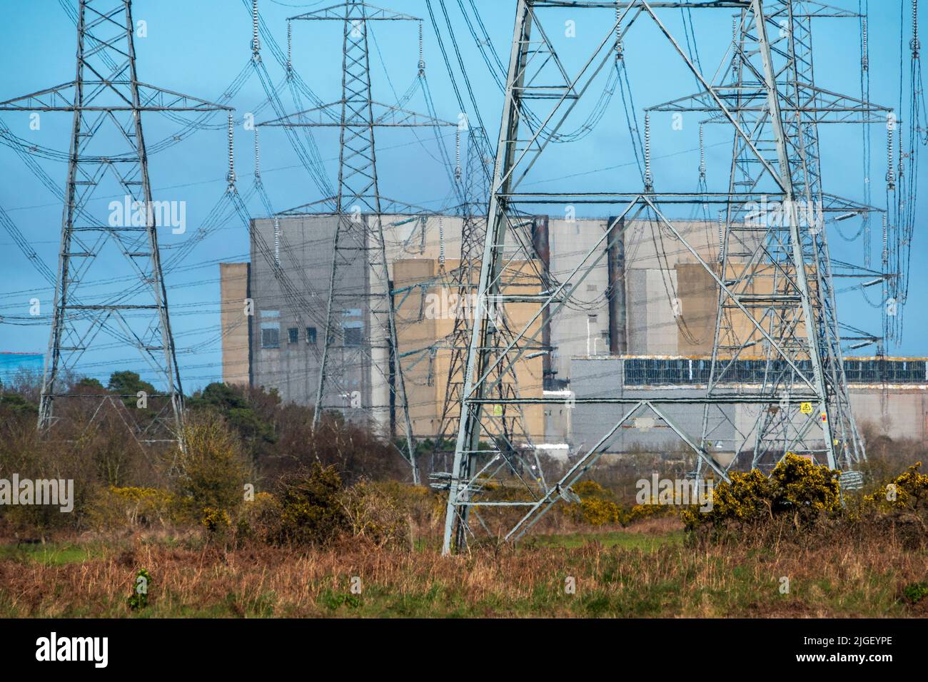 Las centrales nucleares de Sizewell se encuentran a gran distancia, con campos verdes en primer plano y muchas líneas de energía Foto de stock