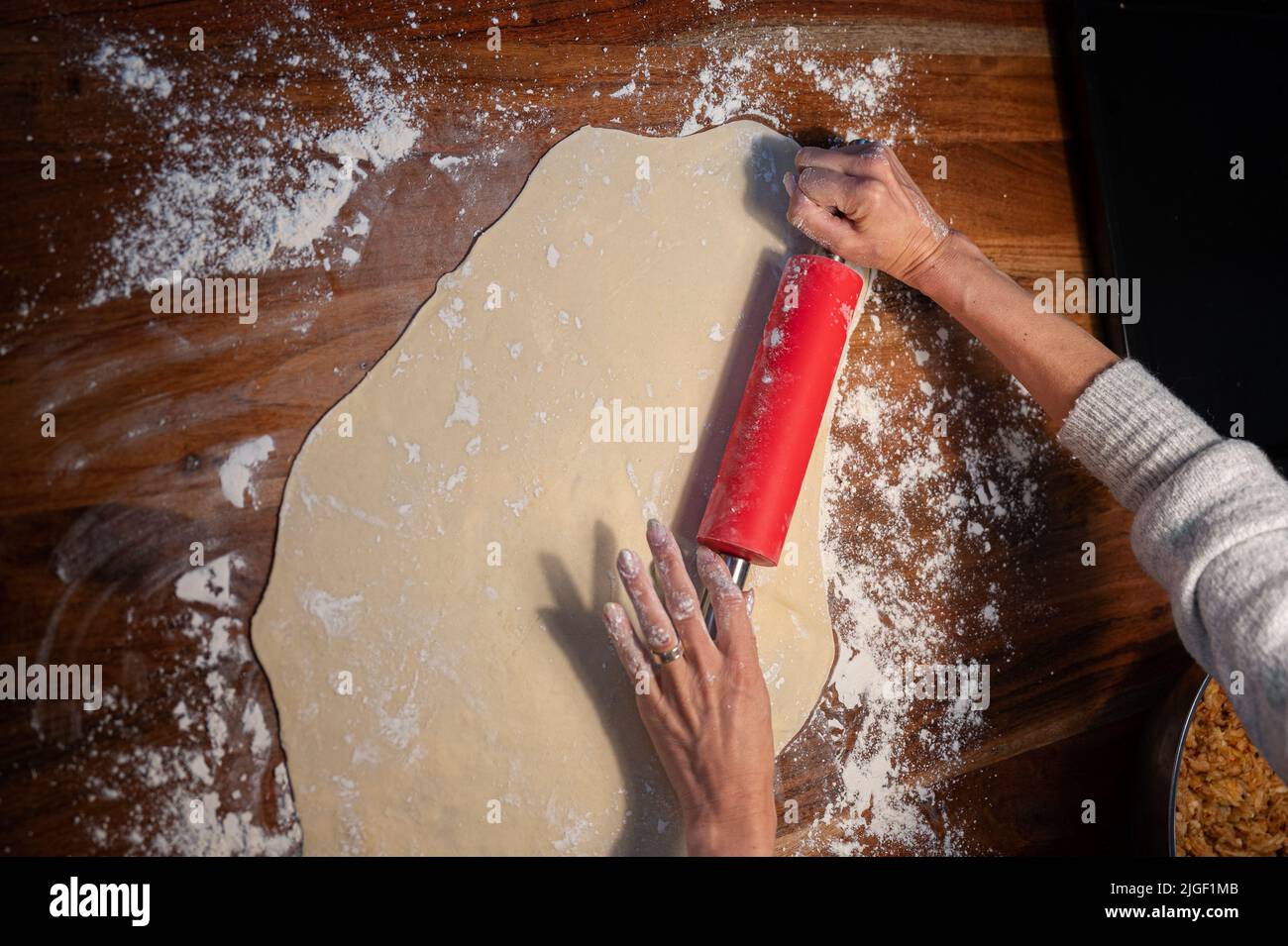 Vista aérea de las manos femeninas rodando masa de pastelería casera con un rodillo en la mesa de comedor nacional. Foto de stock