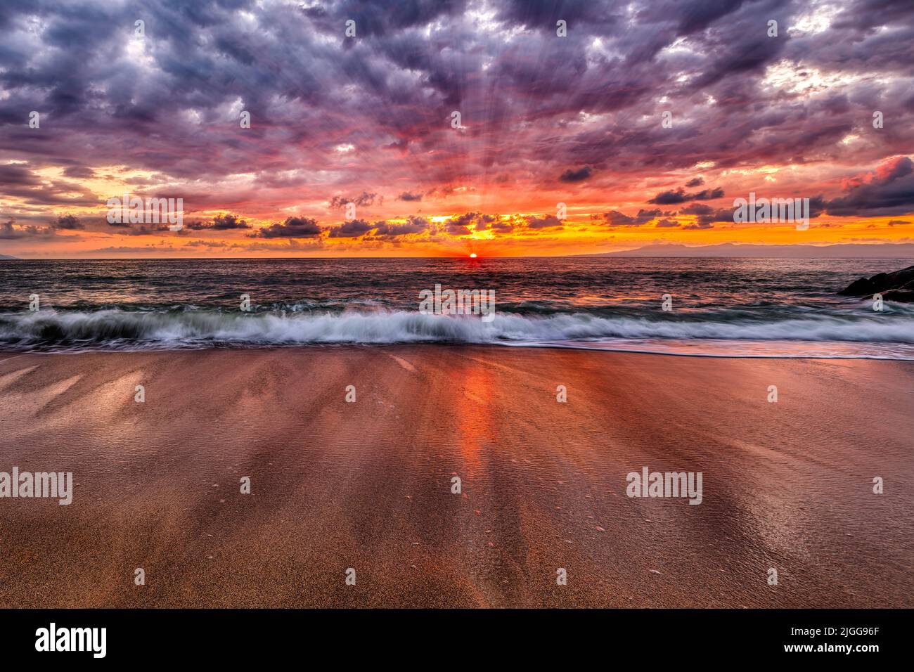 Los rayos del sol están reventando en el horizonte del océano con un vivo y colorido cielo de puesta de sol Foto de stock