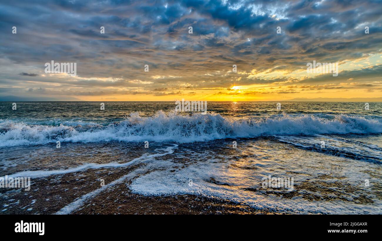 Una ola del océano está rompiendo contra Un colorido cielo de puesta de sol Foto de stock