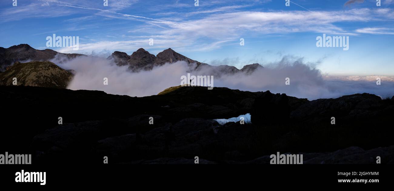 Alto panorama de puesta de sol de montaña con nubes bajas en el valle y persona solitaria, Dolomitas, Lagorai Italia Foto de stock