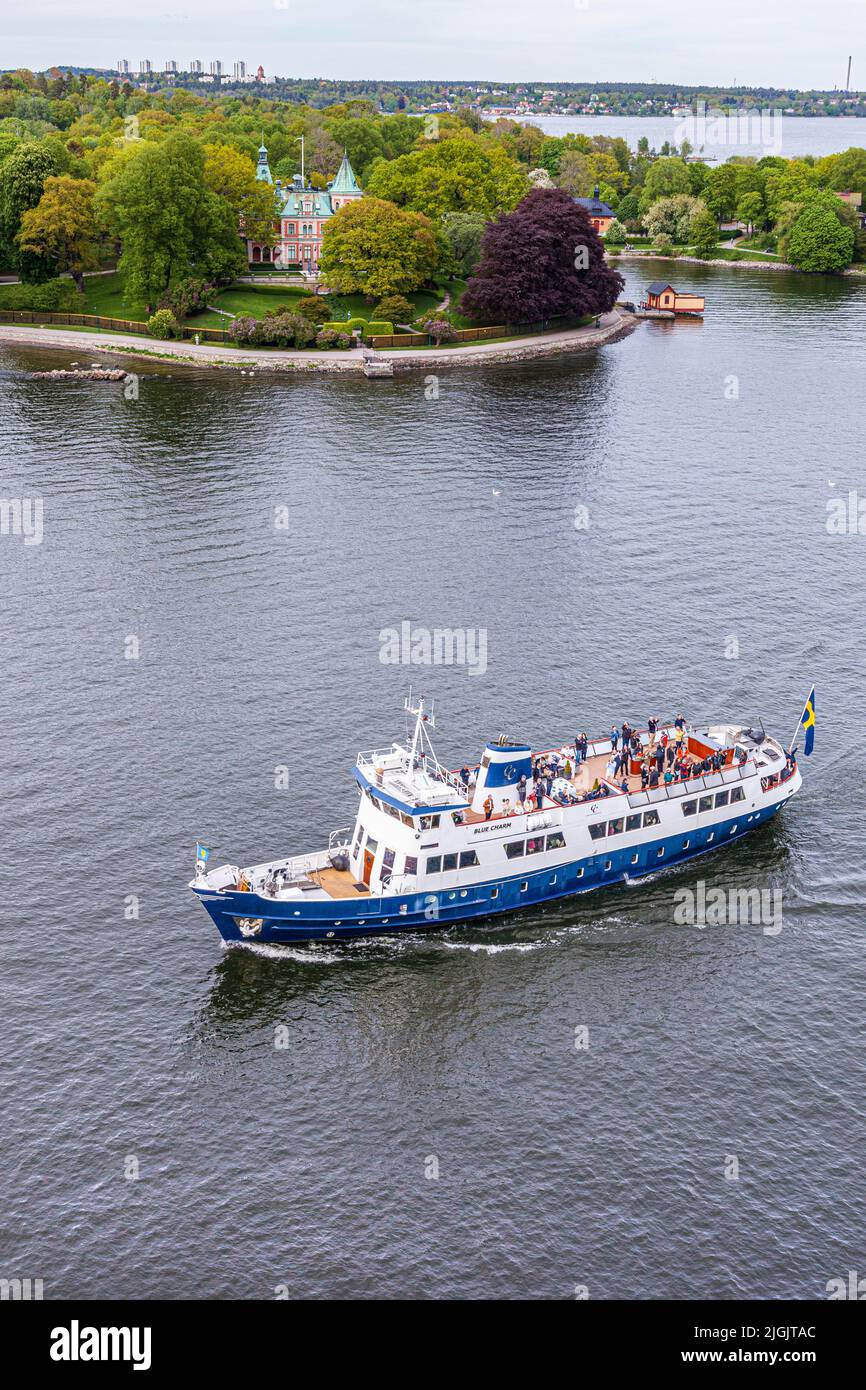 El barco chárter turístico 'Blue Charm' pasando por la villa Takka UDDEN en la isla de Djurgården en el archipiélago de Estocolmo, Suecia Foto de stock