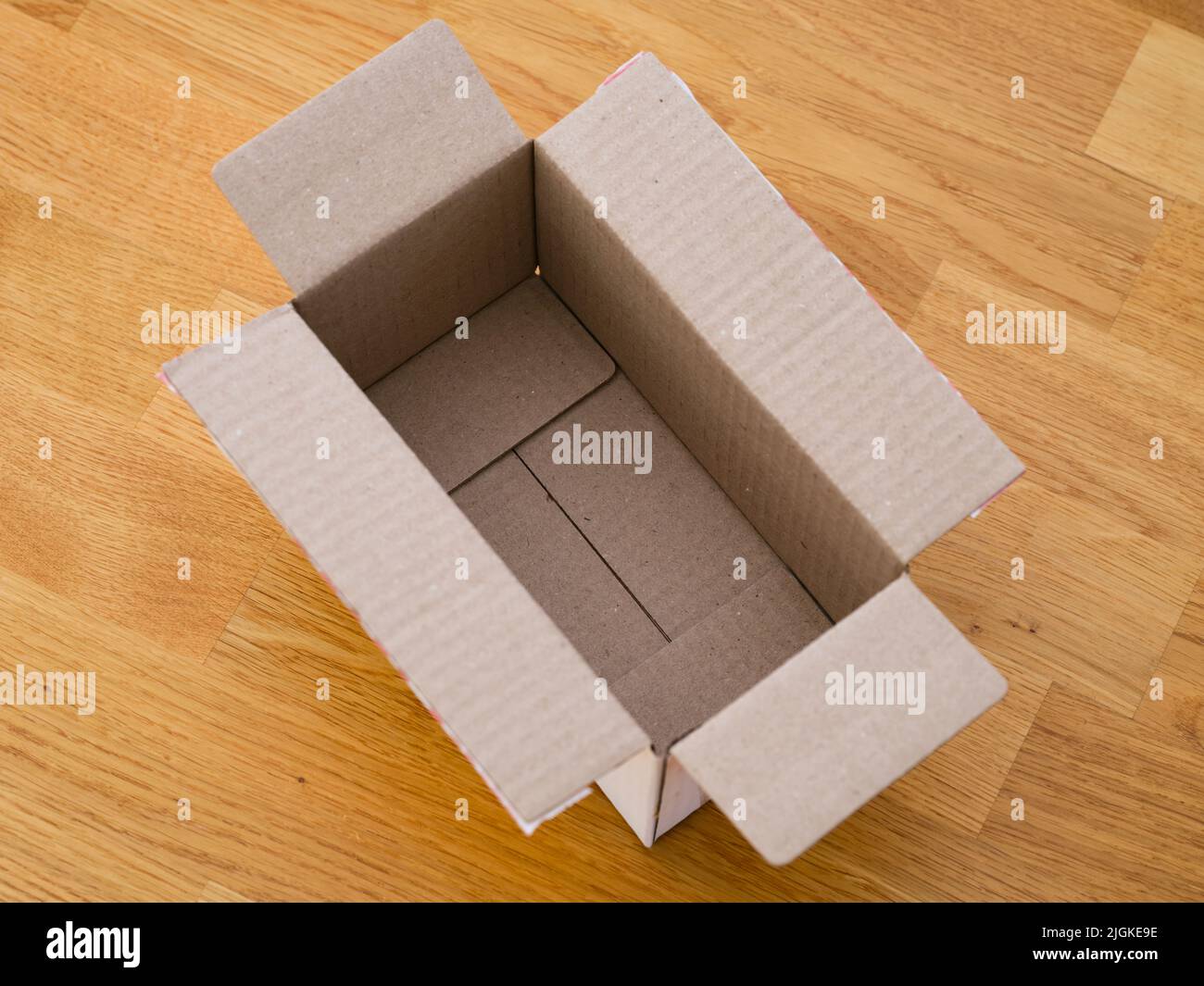 Una caja de cartón abierta vacía sobre un suelo de parqué Foto de stock