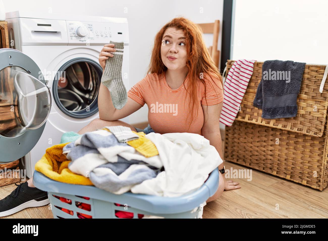 Joven pelirroja poniendo ropa sucia en la lavadora sorprendida con la mano  en la cabeza por error, recuerde el error Fotografía de stock - Alamy