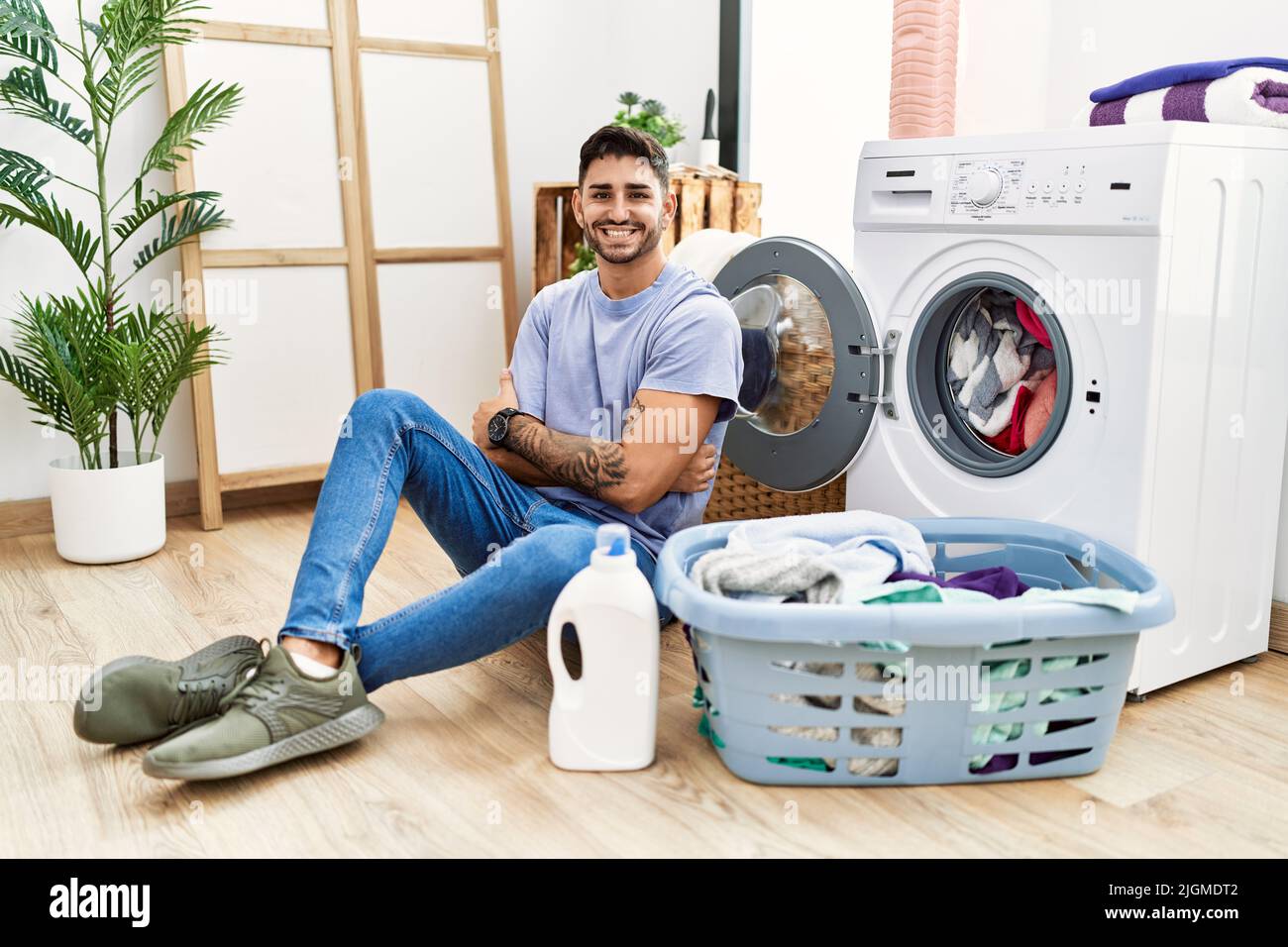 Joven hispano metiendo ropa sucia en la lavadora cara feliz sonriendo con los cruzados mirando la cámara. Persona positiva de stock - Alamy