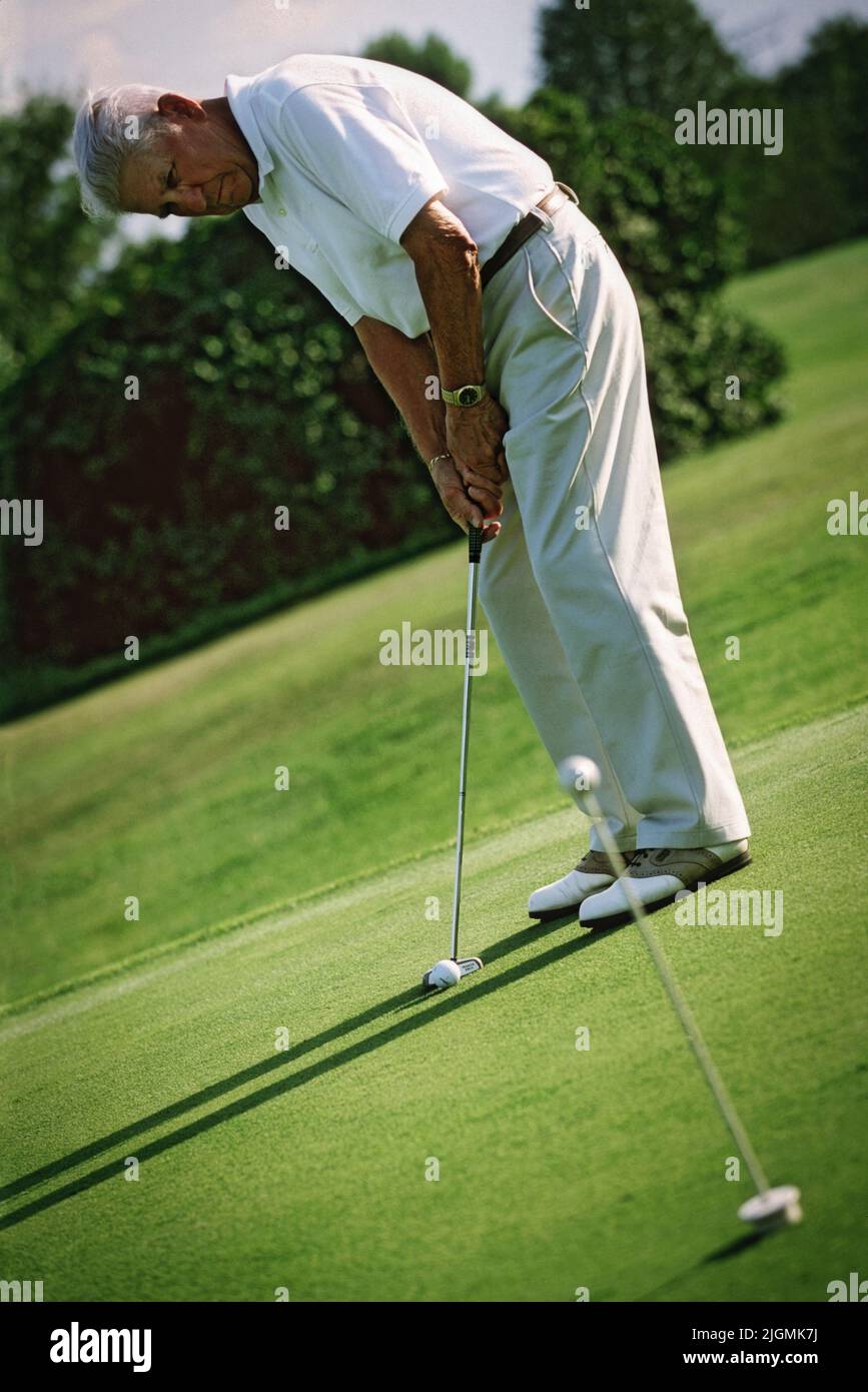Un hombre jubilado practica su puesta en un verde de la práctica para perfeccionar es habilidades. Foto de stock