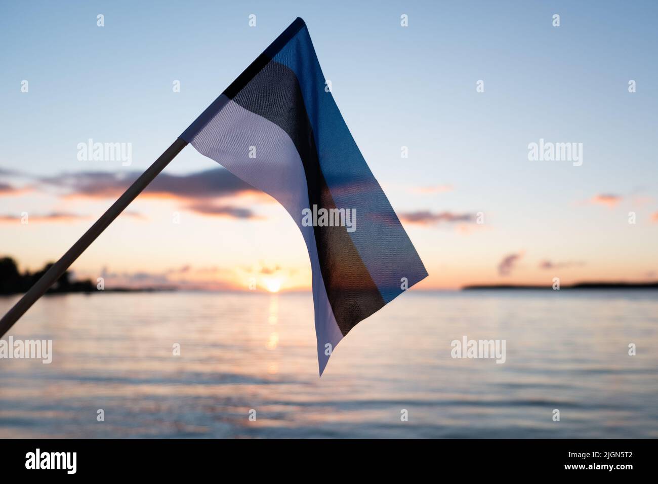 Bandera estonia ondeando al atardecer. Bandera de Estonia en el fondo de la playa de la noche. Foto de stock