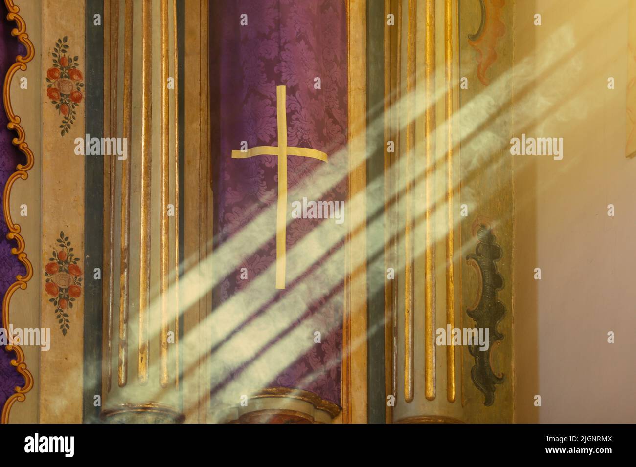 Símbolo religioso con tela de color púrpura con diseño de la cruz que recibe rayos del sol de la luz de la ventana Foto de stock