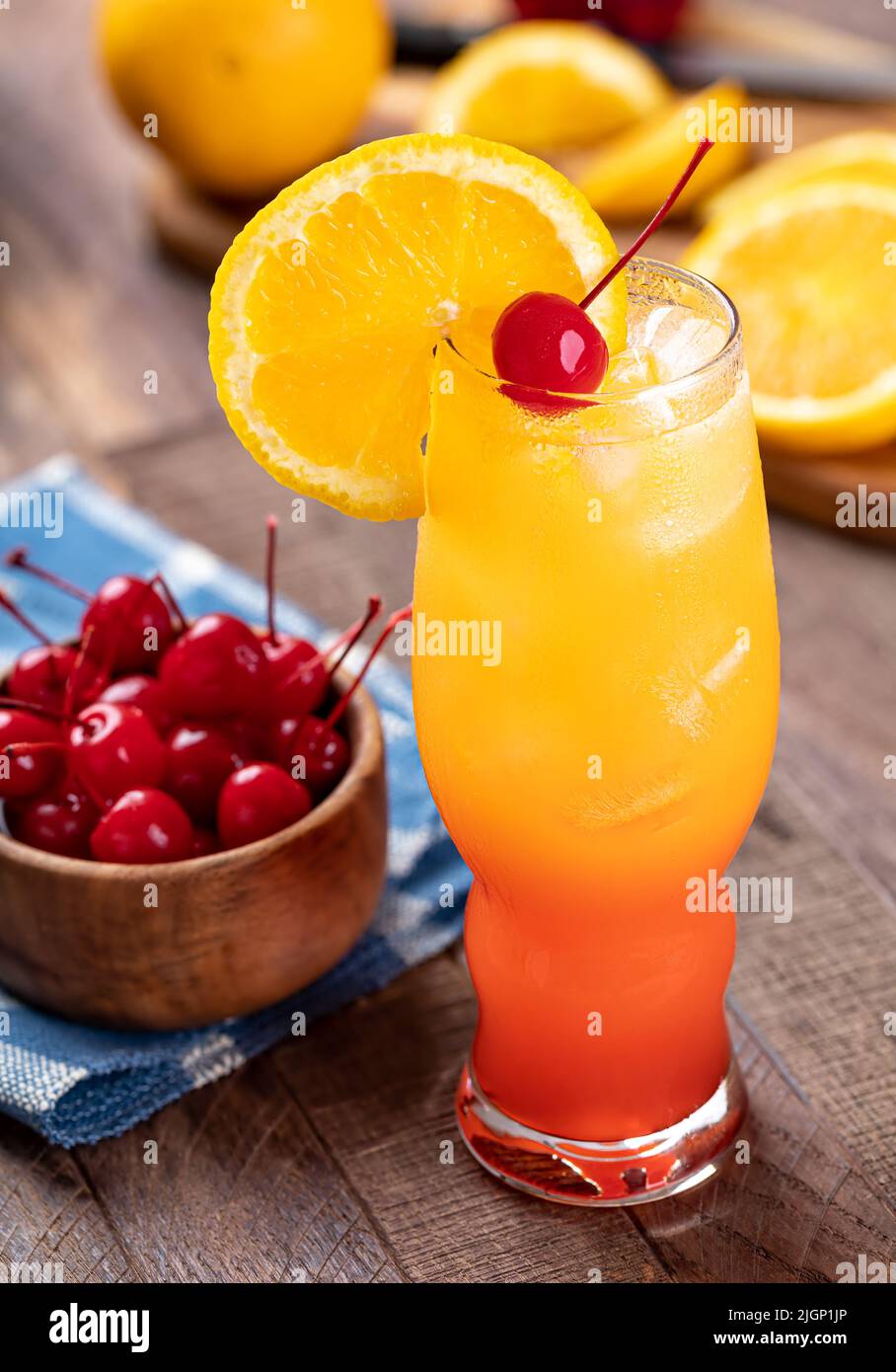 Cóctel Tequila Sunrise con rodaja de naranja y cereza sobre una mesa rústica de madera Foto de stock