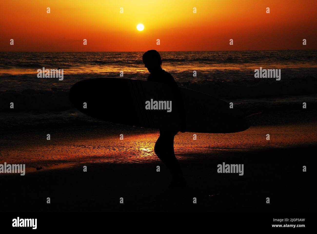 Un joven lleva su tabla de surf a las olas del océano mientras el sol se pone en el Océano Pacífico y California Foto de stock