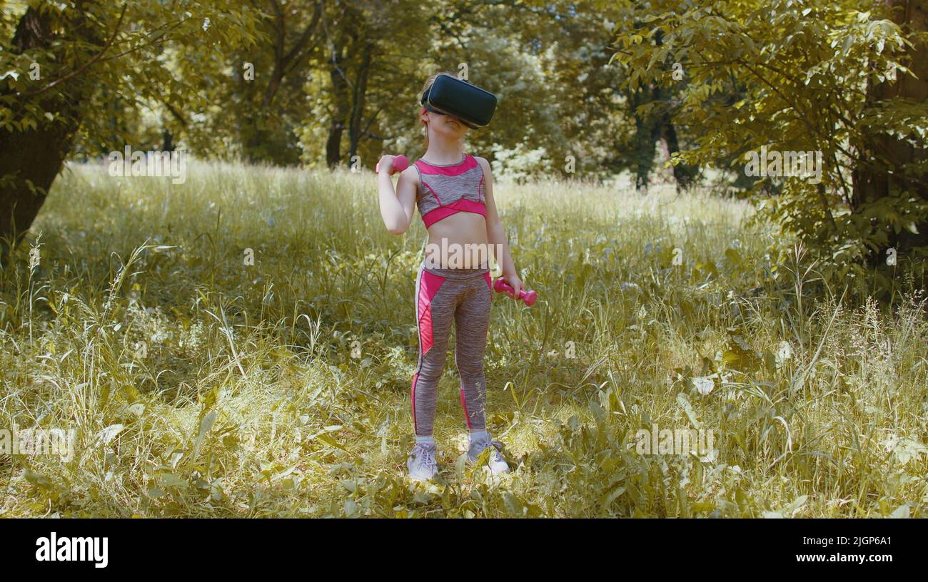 Niño atlético con casco de VR haciendo ejercicios de fitness con pesas al  aire libre en el parque. Entrenamiento online para niños. Pequeña niña  caucásica viendo realidad virtual 3D 360 juego de