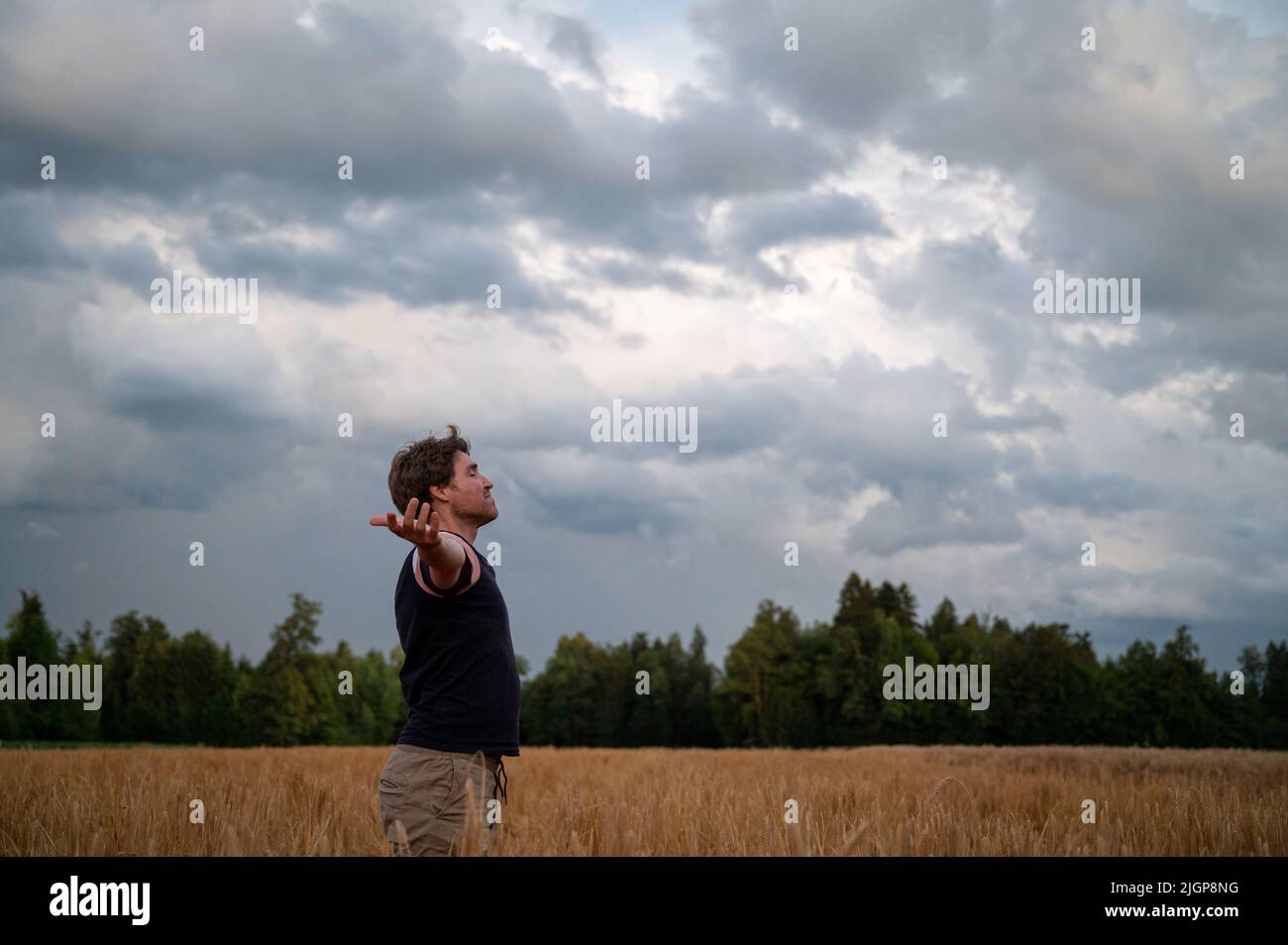 Hombre joven de pie en un hermoso campo de trigo dorado con sus brazos se extendieron practicando la atención plena. Foto de stock