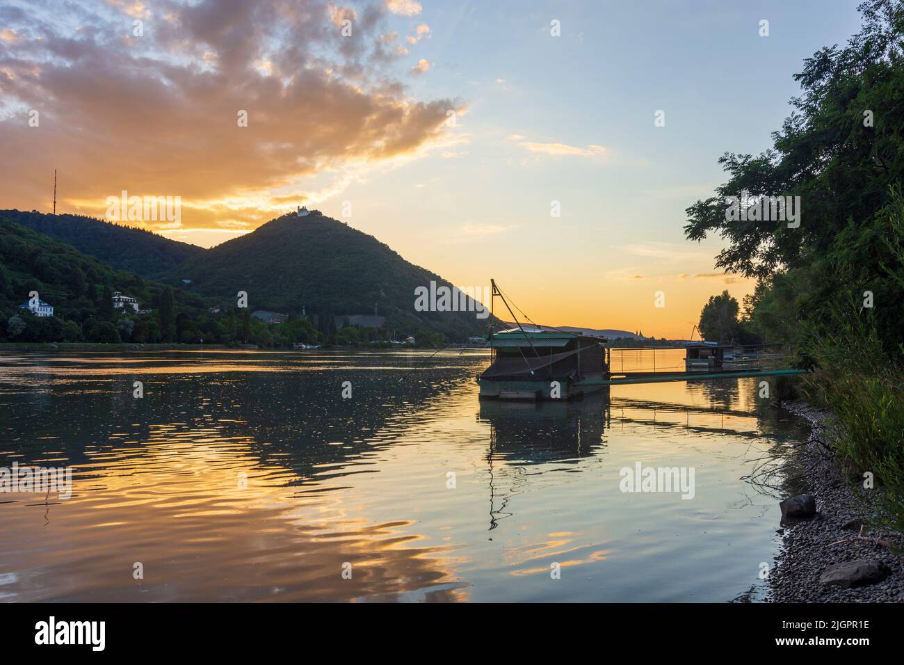 Viena: Puesta de sol en el río Donau (Danubio), vista a la montaña Kahlenberg (izquierda) y Leopoldsberg (con iglesia), barco Daubel con red de pesca Foto de stock