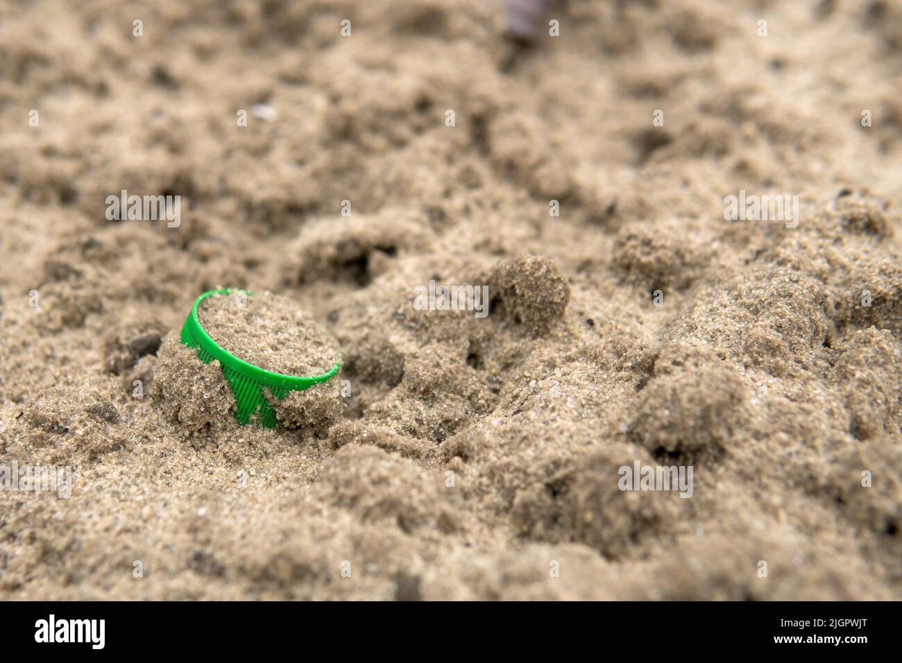 Un corcho verde de una botella de plástico yace en la arena. Contaminación ambiental con residuos plásticos. Concepto de protección de la naturaleza. Guardar la ecología para las generaciones futuras. Foto de stock