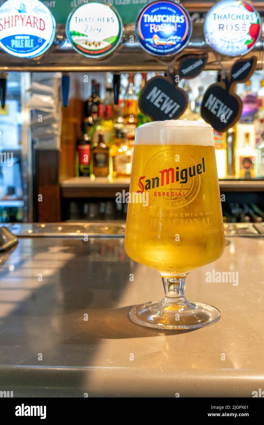 Una pinta completa de lager de San Miguel o cerveza con la cabeza espumosa en un vaso de la marca San Miguel en el mostrador del bar de un pub JD Wetherspoons Foto de stock