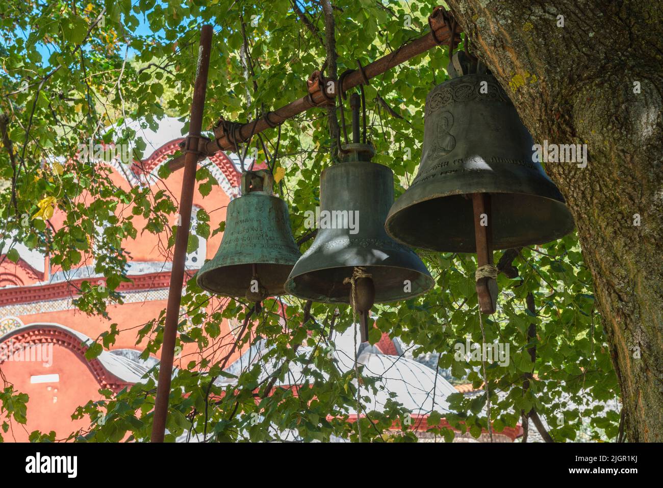 Tres campanas de bronce colgando bajo un árbol fuera del monasterio medieval ortodoxo serbio Patriarcado de Peć en Kosovo. Foto de stock