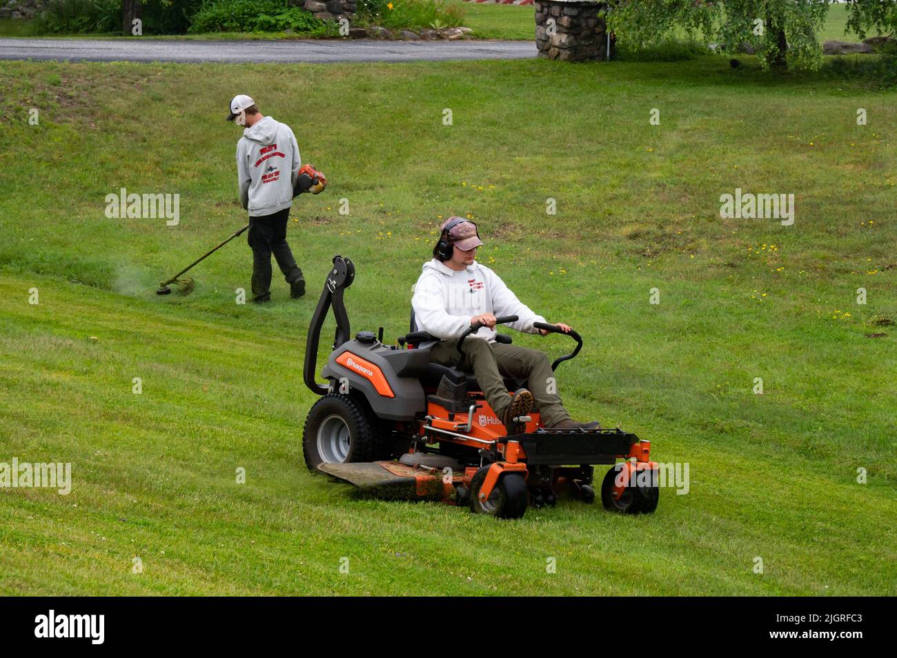 Dos hombres con un servicio de césped segando y recortando con un tractor de césped y cortapatillas de malas hierbas Foto de stock