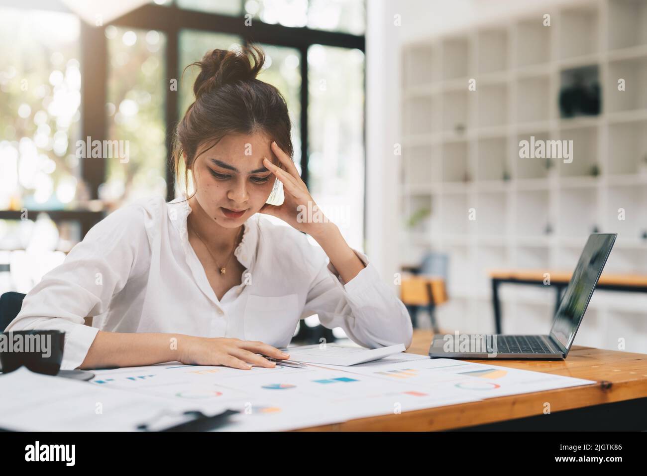 Joven asiática Trabajadora de Oficina utiliza el ordenador portátil, se siente explosión repentina de dolor, dolor de cabeza, migraña. Sobretrabajado Contador Sensación Proyecto Presión, estrés Foto de stock