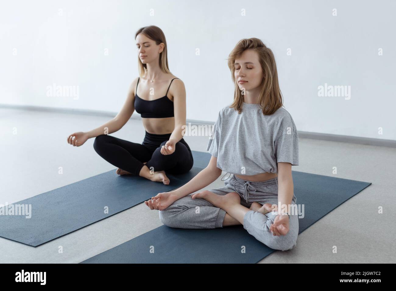 Dos muchachas atractivas atléticas se sientan en posición del loto en la estera del yoga adentro .Yoga, aptitud y forma de vida sana Foto de stock