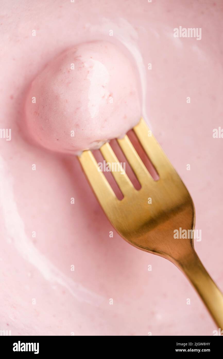 Vista conceptual de primer plano de la bola de queso dulce en un tenedor dorado con salsa de bayas rosadas. Foto de stock