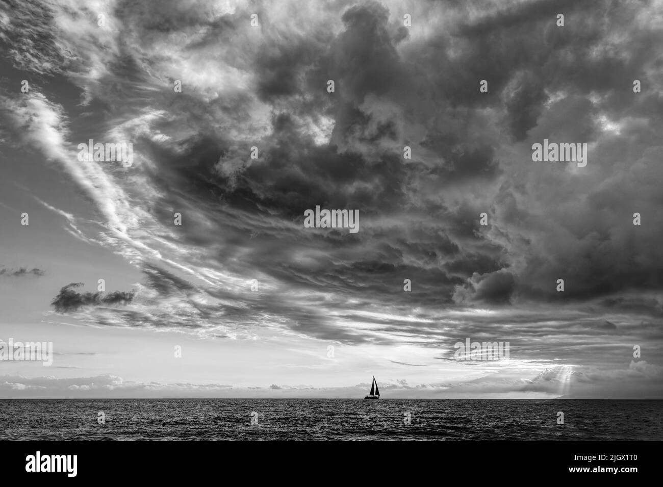 Una tormenta se avecina mientras Un pequeño barco se mueve a lo largo del horizonte del océano en blanco y negro Foto de stock
