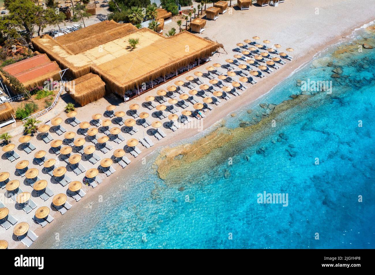 Vista aérea de la playa de arena con sombrillas, árboles verdes al atardecer Foto de stock
