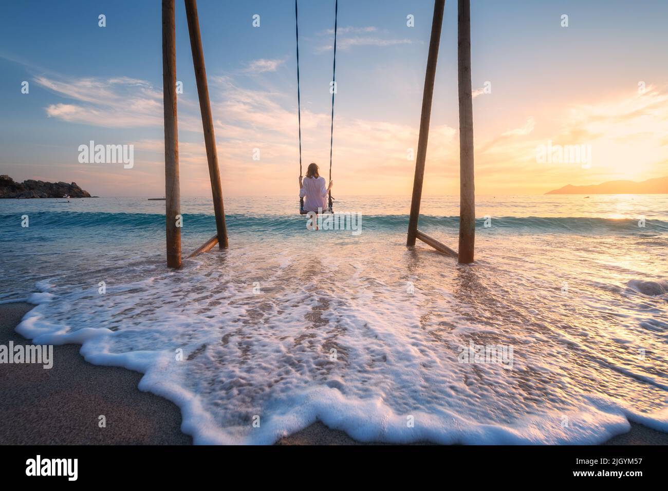 Mujer joven feliz en el columpio de madera en el agua, el mar con las olas Foto de stock