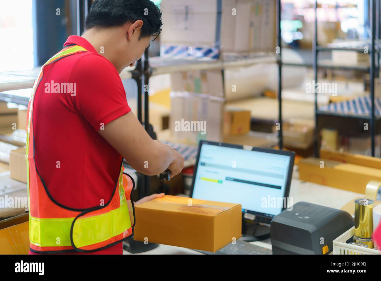 Trabajador de almacén asiático con ordenador y escáner de código de barras en el almacén escáner en la caja preparar la entrega al cliente. Foto de stock