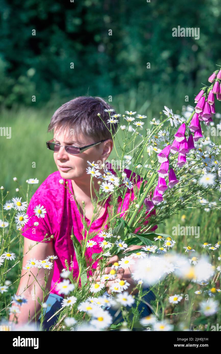 Mujer colecciona un ramo de flores silvestres con margaritas y guantes de foxglove Foto de stock