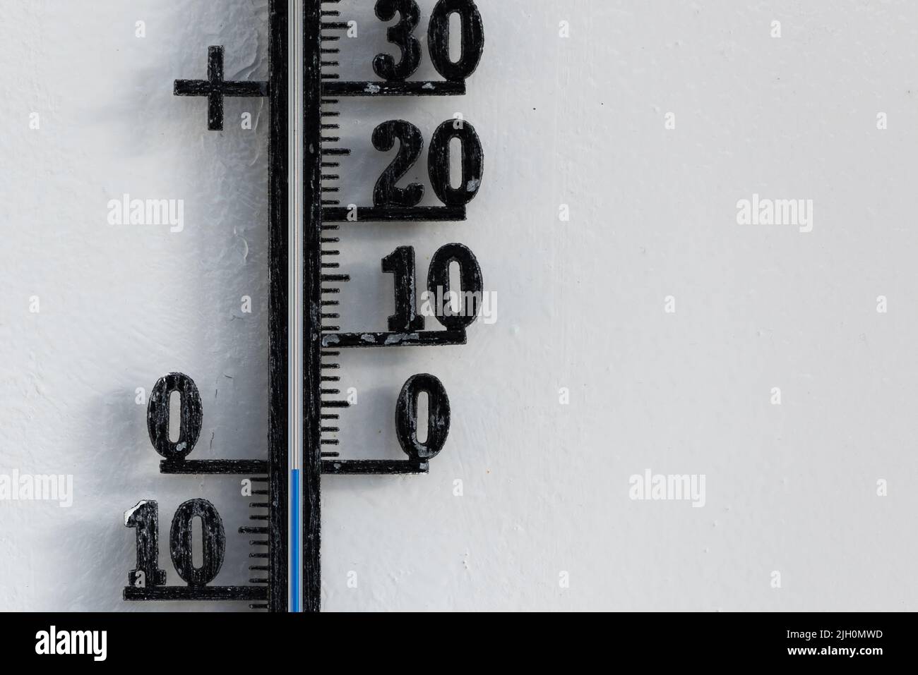 Termómetro analógico negro clásico colgado en la pared blanca que muestra una escala de temperatura azul de cero, 0 grados centígrados Foto de stock