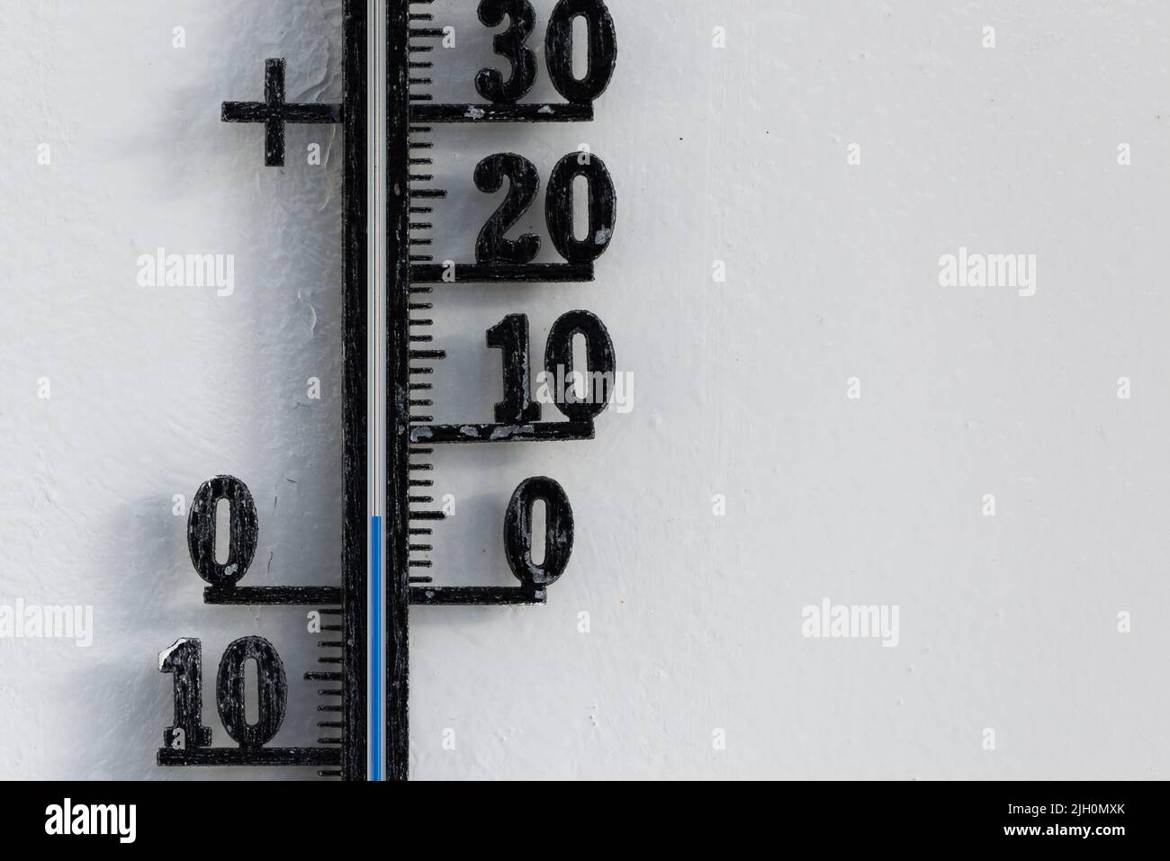 Termómetro analógico negro clásico colgado en una pared blanca que muestra una escala de temperatura azul de cinco, 5 grados centígrados Foto de stock