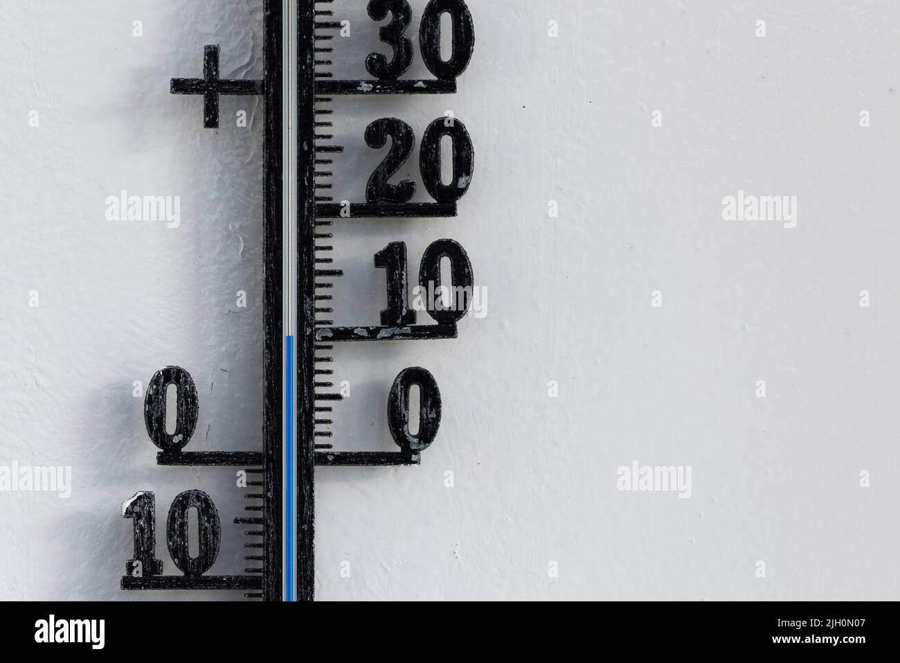 Termómetro analógico negro clásico colgado en una pared blanca que muestra una escala de temperatura azul de diez, 10 grados centígrados Foto de stock