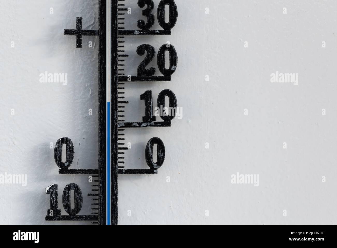 Termómetro analógico negro clásico colgado en una pared blanca que muestra una escala de temperatura azul de 15, quince grados centígrados Foto de stock