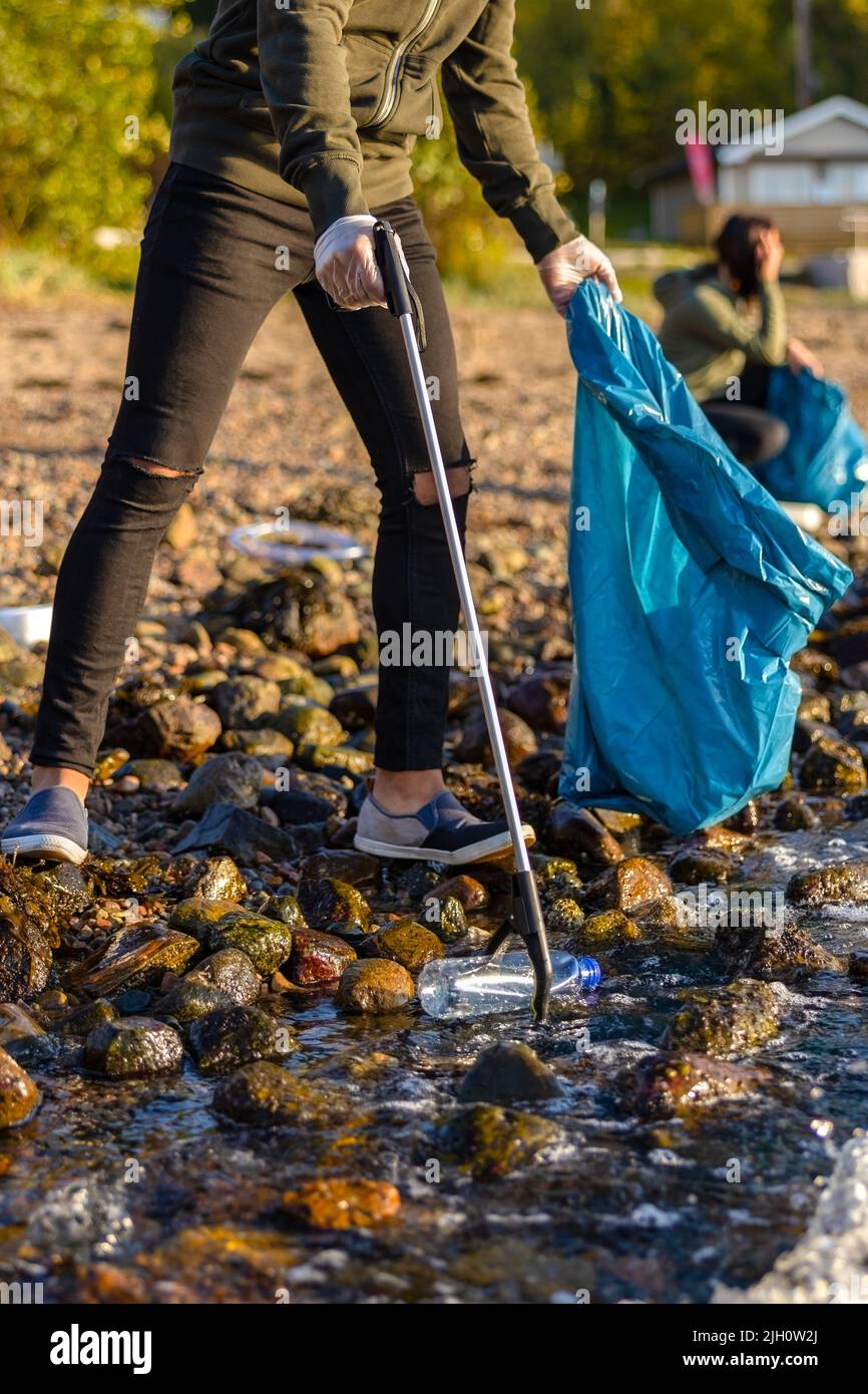 Primer plano de voluntarios recogiendo basura con agarrador en la playa Foto de stock